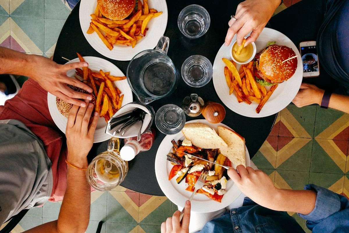 Friends sharing burgers, fries and roasted vegetables around a table