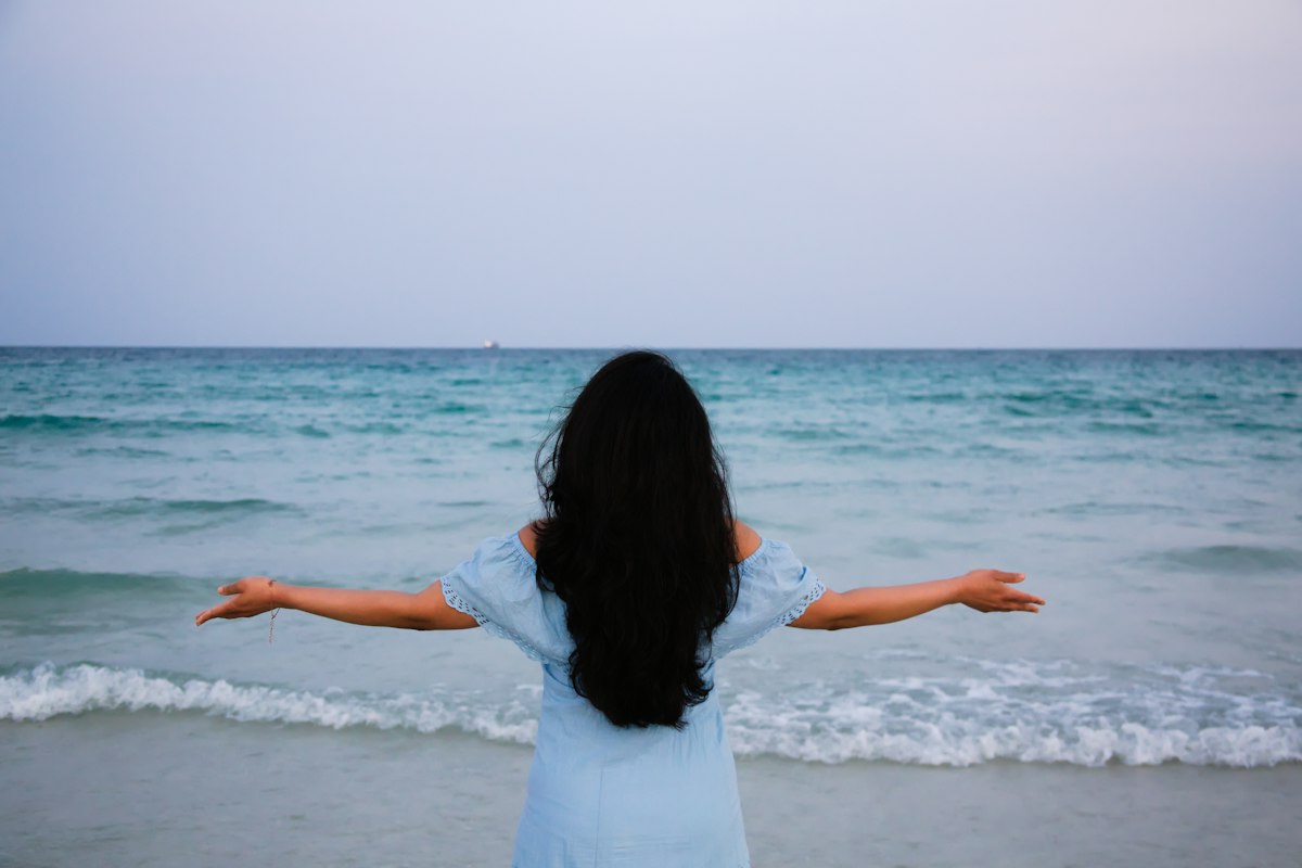 A woman standing at the water's edge with her arms open wide