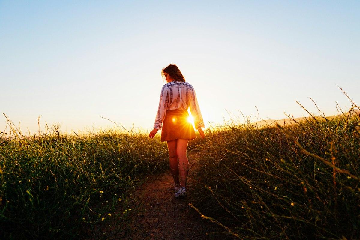 A woman walking through a field at sunset
